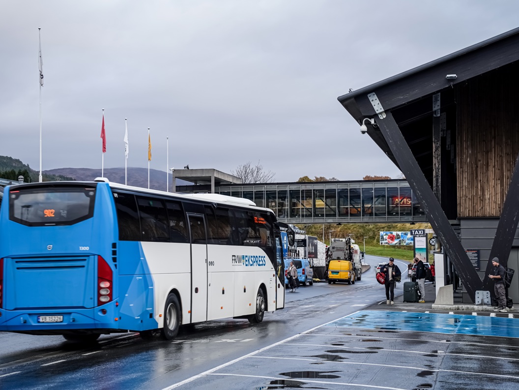 Flybuss på Molde lufthavn, folk med bagasje på perrongen, moderne arkitektur i bakgrunnen.