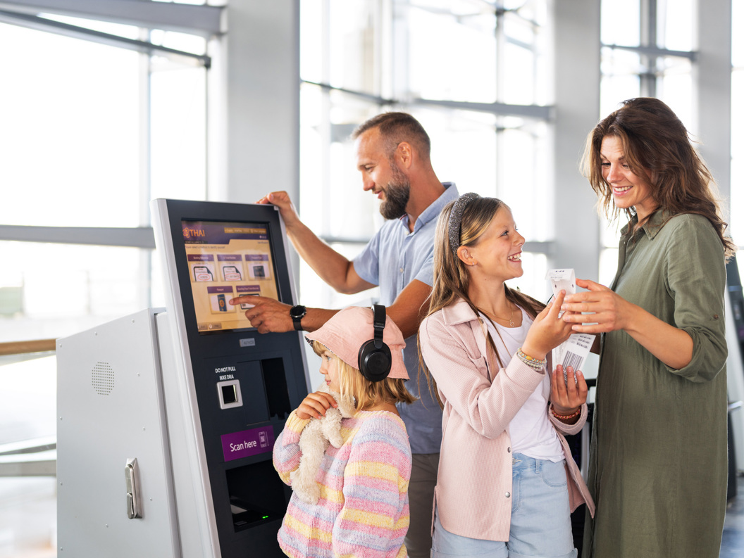 Familie ved innsjekkingsautomat på flyplass, med mor, far og to barn som sjekker inn billetter på en digital terminal. Atmosfære av reiseglede og moderne teknologi.
