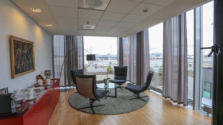 Lyst møterom med utsikt over flyplass, elegant innredet med moderne stoler, et rundt bord og kunst på veggen.