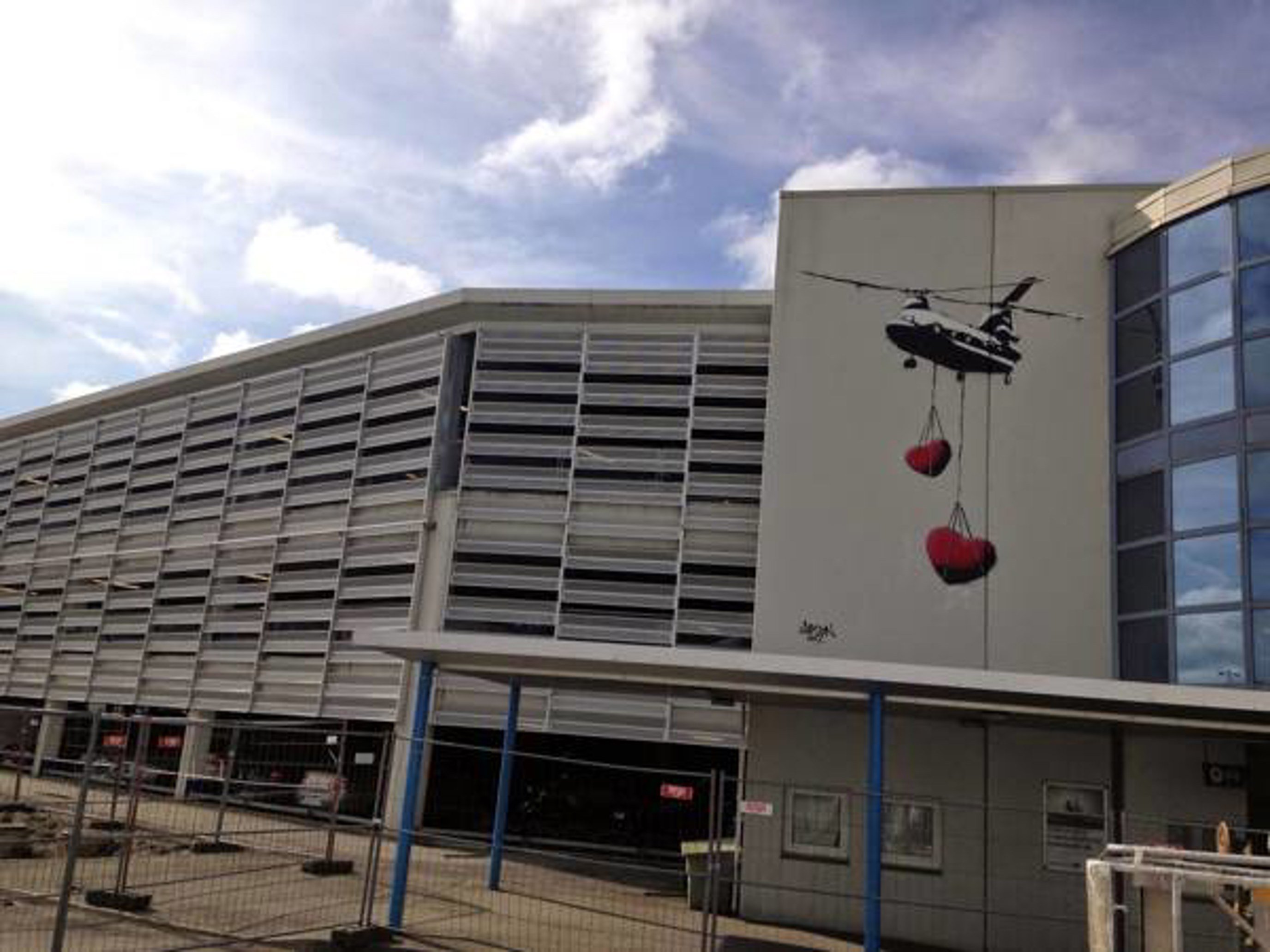 Kunstverk på Stavanger flyplass, maleri utenpå terminalbygget. To hjerter i rødt henger fra et fly